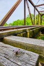 Cross shaped nail sticking out of wooden beam on long truss iron metal railroad bridge with tracks
