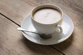 Image of a cup of coffee on a suacer with an old vintage spoon and a vanilla cookie, placed on a wooden table top