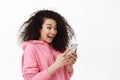Image of curly girl look surprised at mobile phone screen, receive exciting news message on smartphone, chatting in app Royalty Free Stock Photo