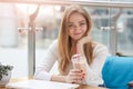 Image of cute adorable femal looking directly at camera, having lunch in cafeteria, holding plastic cup of milkshake, putting