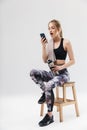 Image of cute blond woman 20s dressed in sportswear using smartphone while sitting on chair after workout in gym Royalty Free Stock Photo