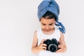 Image of cute little girl wearing turban on the head holding an photo camera, isolated on white background. Adorable child taking Royalty Free Stock Photo