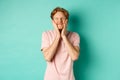 Image of cute and silly young man with red hair, feeling satisfaction while touching his face, smiling happy, standing Royalty Free Stock Photo