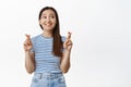 Image of cute young woman praying, making wish, fingers crossed and look at upper right corner with hopeful smile