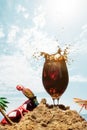 Image of dark cool beer, glass standing into sand over sea and sky background. Summertime chill, beer splash Royalty Free Stock Photo