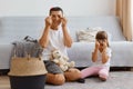Image of dark haired male with his female child playing together at home, sitting on floor near cough in light room, making Royalty Free Stock Photo