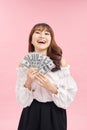Image of delighted woman wearing basic clothes smiling and holding money cash isolated over pink background
