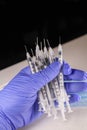 Image is depicting a handful of syringes by a medical professionals gloved hand.