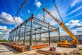 Construction site with cranes assembling steel frame of a building and workers on the ground Royalty Free Stock Photo