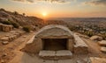 stone cave with dome-shaped opening sits atop rocky hillside, overlooking cityscape at sunset. Royalty Free Stock Photo