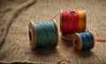 Three spools thread in blue, red, and yellow are arranged on textured fabric surface.