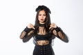 Image of disappointed asian woman in halloween dress of gothic undead girl showing thumbs-down, dislike and disagree