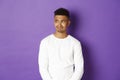 Image of disappointed and sad african-american man, looking left and grimacing, standing over purple background Royalty Free Stock Photo