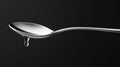 The image displays a sleek silver spoon capturing a droplet of liquid at its tip, set against a deep black background that Royalty Free Stock Photo