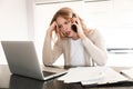 Displeased blonde woman posing sitting indoors at home using laptop computer talking by mobile phone Royalty Free Stock Photo