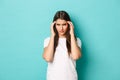 Image of distressed young woman trying to focus, touching head and squinting, having headache, standing over blue