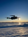 An image of a drone flying at sunset over a snowy landscap