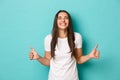 Image of ecstatic brunette girl, feeling happy and lucky, smiling pleasured while showing thumbs-up, standing amazed