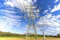 Image of an electricity pylon from the ground perspective in front of a blue sky with white clouds Royalty Free Stock Photo