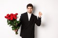 Image of elegant and sassy man in black suit, looking confident and holding bouquet of red roses, going on a romantic