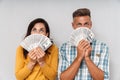 Emotional adult loving couple holding money isolated over grey wall background covering face