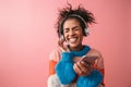 Emotional beautiful young african woman posing  over pink wall background listening music with headphones Royalty Free Stock Photo