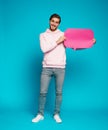 Image of emotional excited young man posing isolated over light blue wall background holding speech bubble Royalty Free Stock Photo