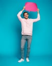 Image of emotional excited young man posing isolated over light blue wall background holding speech bubble Royalty Free Stock Photo