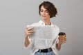 Emotional young business woman posing isolated over grey wall background reading newspaper drinking coffee Royalty Free Stock Photo