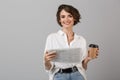 Emotional young business woman posing over grey wall background reading newspaper drinking coffee Royalty Free Stock Photo