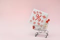 Image of empty shopping trolley or cart with box of discount percent sale black Friday products on pink background