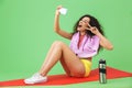 Image of energetic girl 20s in sportswear with towel over neck taking selfie photo while sitting on fitness mat after workout