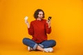 Image of european woman using cell phone and credit card while sitting on the floor isolated over yellow background Royalty Free Stock Photo