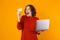 Image of european woman using silver laptop and credit card while standing isolated over yellow background Royalty Free Stock Photo