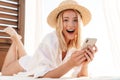 Image of excited blonde woman using cellphone while lying on bed Royalty Free Stock Photo