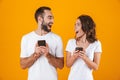 Image of excited couple man and woman smiling while both using mobile phones, isolated over yellow background Royalty Free Stock Photo