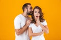 Image of excited man whispering secret or interesting gossip to woman in her ear, isolated over yellow background