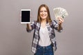 Image of excited young lady isolated over blue background. Looking camera showing display of tablet computer holding money Royalty Free Stock Photo