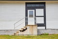 Exterior white house with white door with stained glass mosaic windows and busted concrete steps