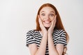 Image of extremely happy and surprised young woman with red hair, touching face and smiling amazed, receiving surprise Royalty Free Stock Photo