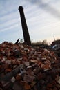 Factory smoke tower silhouetted against the sky with large piles of bricks in the foreground