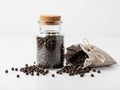 A glass jar filled with black peppercorns sits next to a burlap sack on a white surface Royalty Free Stock Photo