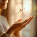 A person holds a small wind turbine model in their hands. This image symbolizes sustainable energy and innovation. The Royalty Free Stock Photo