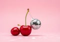 A shiny disco ball nestled between two vibrant red cherries on a pink background Royalty Free Stock Photo