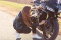 Image of female biker wears black clothes and white sneakers, repairs motorbike, stands on road, solves problem on road, likes