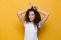 Image of flirting european woman 20s with curly hair showing rabbit ears at her head, isolated over yellow background Royalty Free Stock Photo