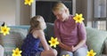 Image of flowers over caucasian mother and daughter talking and smiling on sofa Royalty Free Stock Photo