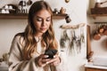 Image of focused caucasian woman using smartphone in cozy kitchen