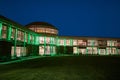 Front view of a dormitory at a university with green lighting the facade and lots of windows at night