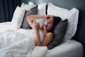 Image of frustrated upset woman 20s with dark hair lying in bed on white pillow after sleep and looking at modern mobile